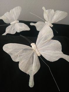 three white butterflies sitting on top of a black cloth covered table with sequins