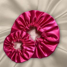 two pink scrunffles sitting on top of a white satin bed spreader