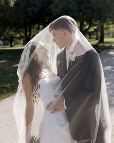 a bride and groom standing together in the street with their veil over their heads, looking at each other