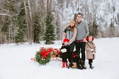 a family is posing for a photo in the snow with presents and christmas tree decorations