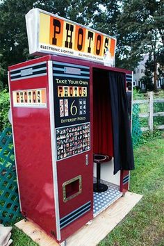 an old fashioned photo booth is in the grass near a fence and some trees with red curtains on it