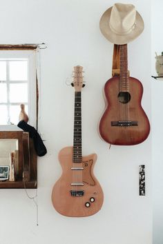 two guitars are hanging on the wall next to a mirror with a cowboy hat on it