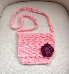 a pink crocheted purse with a flower on the front and side, sitting on a white surface