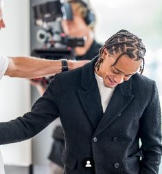 a man with dreadlocks getting his hair styled by another man in a white t - shirt and black blazer