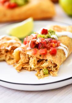 a white plate topped with two tacos covered in sauce and toppings next to an apple