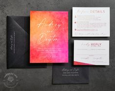 the wedding stationery is laid out on top of each other, including an orange and pink watercolored paper