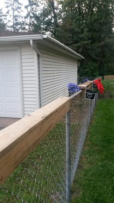 a fence with flowers growing on it next to a house and garage in the background