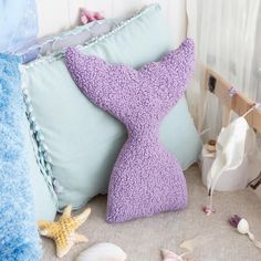 a purple mermaid tail pillow sitting on top of a bed next to pillows and seashells