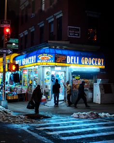 people walking in front of a deli grocery store on a city street at night