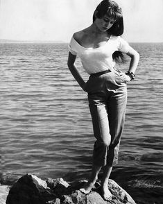 a woman standing on top of a rock next to the ocean with her hands on her hips