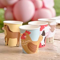 four cups with farm animals on them sitting on a wooden table in front of balloons