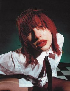 a woman with red hair wearing a white shirt and tie sitting on a checkered floor