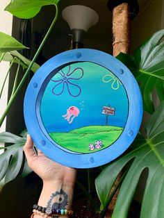 a hand holding up a painted plate with an elephant on it's side and a street sign in the background