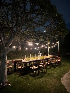 an outdoor dinner table set up with lit candles and greenery under a tree at night