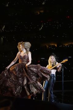 two women are performing on stage with one holding a guitar and the other standing behind her