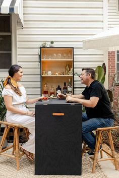 a man and woman sitting at an outdoor bar with drinks in front of the back door