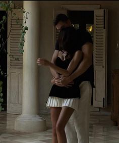 a man and woman embracing each other in the middle of a room with white columns