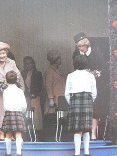 an older woman and two young children standing in front of a group of people wearing kilts