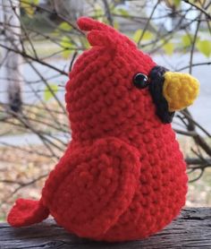 a crocheted red bird sitting on top of a wooden table next to a tree