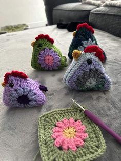 four crocheted chickens sitting on top of a bed next to a knitting needle