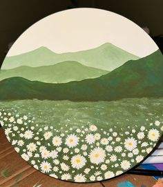 a painted plate with daisies in the foreground and mountains in the back ground