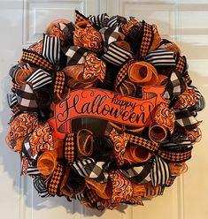 a wreath that says happy halloween on the front door with orange, black and white ribbons