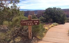 a trail sign on the side of a dirt road with trees and mountains in the background