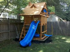 a wooden playset with a blue slide in the back yard next to a fence