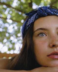 a young woman wearing a bandana looking up at the camera with trees in the background