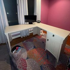 a white desk sitting in front of a window next to a trash can and computer monitor