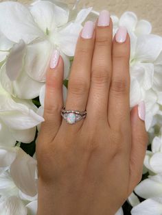 a woman's hand with a ring on top of her finger and flowers in the background