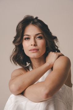 a woman in a white dress posing for a photo with her arms folded over her chest