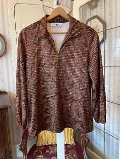 This top from Golden Wings is made from 100 per cent polyester in an abstract pattern in black with light brown and coppery brown tones. It has a pointy collar with a slight v neck and elastic at the cuffs. Marked size 38. The measurements, taken with the shirt lying flat, are: shoulder to shoulder, 18 inches; armpit to armpit, 23 inches; sleeves, 24 inches; length, 24 inches; bottom edge, 24 inches. In very good condition. Pointy Collar, Fabric Print Design, Golden Wings, Brown Tones, Pullover Shirt, Grey Top, Vintage Brown, Print Top, Print Tops