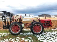 an old red tractor parked in the middle of a field with snow on the ground