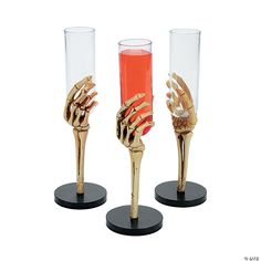 three gold colored vases with hands on each one holding a red liquid in it