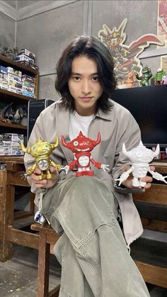 a young man sitting on a chair holding three toy figures in his hands and looking at the camera