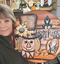 a woman standing next to a sign that says pumpkins for sale with an image of a scarecrow on it