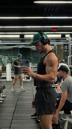 a man standing in a gym with headphones on while looking at his cell phone