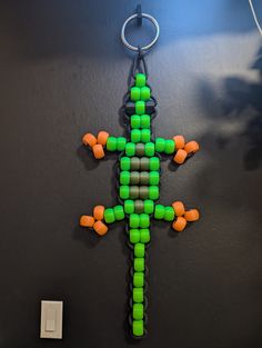 a green and orange beaded lizard hanging from a hook on a black wall next to a light switch