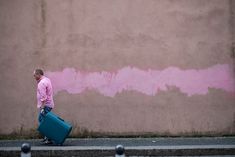 a man walking down the street carrying a blue suitcase with pink paint painted on it