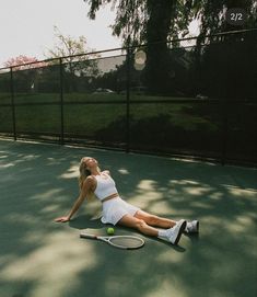 a woman laying on the ground with a tennis racket in her hand while holding a tennis ball