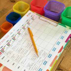 a close up of a pen on top of a paper with colored cups in the background