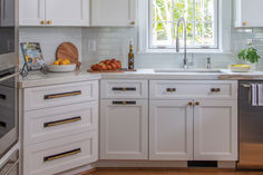 a kitchen with white cabinets and gold pulls on the handles, an oven door, and a dishwasher