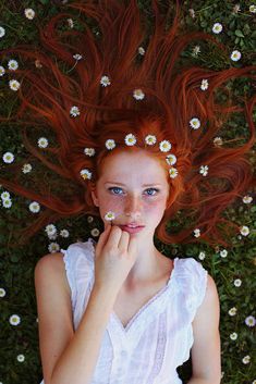 a woman with red hair laying on the ground surrounded by daisies