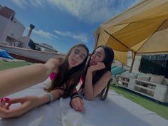 two young women laying on top of a blanket next to each other in front of a tent