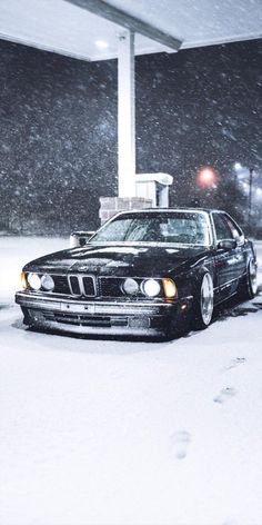 a black car parked in the snow at a gas station with it's lights on