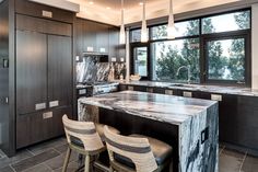 a large kitchen with marble counter tops and dark wood cabinets, along with two bar stools