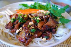 a white plate topped with meat, noodles and veggies next to carrots