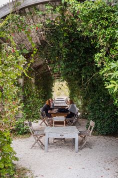 two people sitting at a picnic table under an arch in the middle of a garden