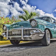 an old classic car parked on the side of the road with palm trees in the background